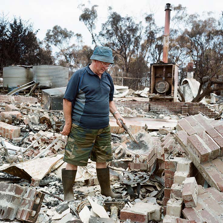 An older man walks across the burnt rubble of his house