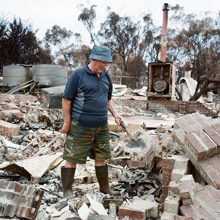 An older man walks across the burnt rubble of his house