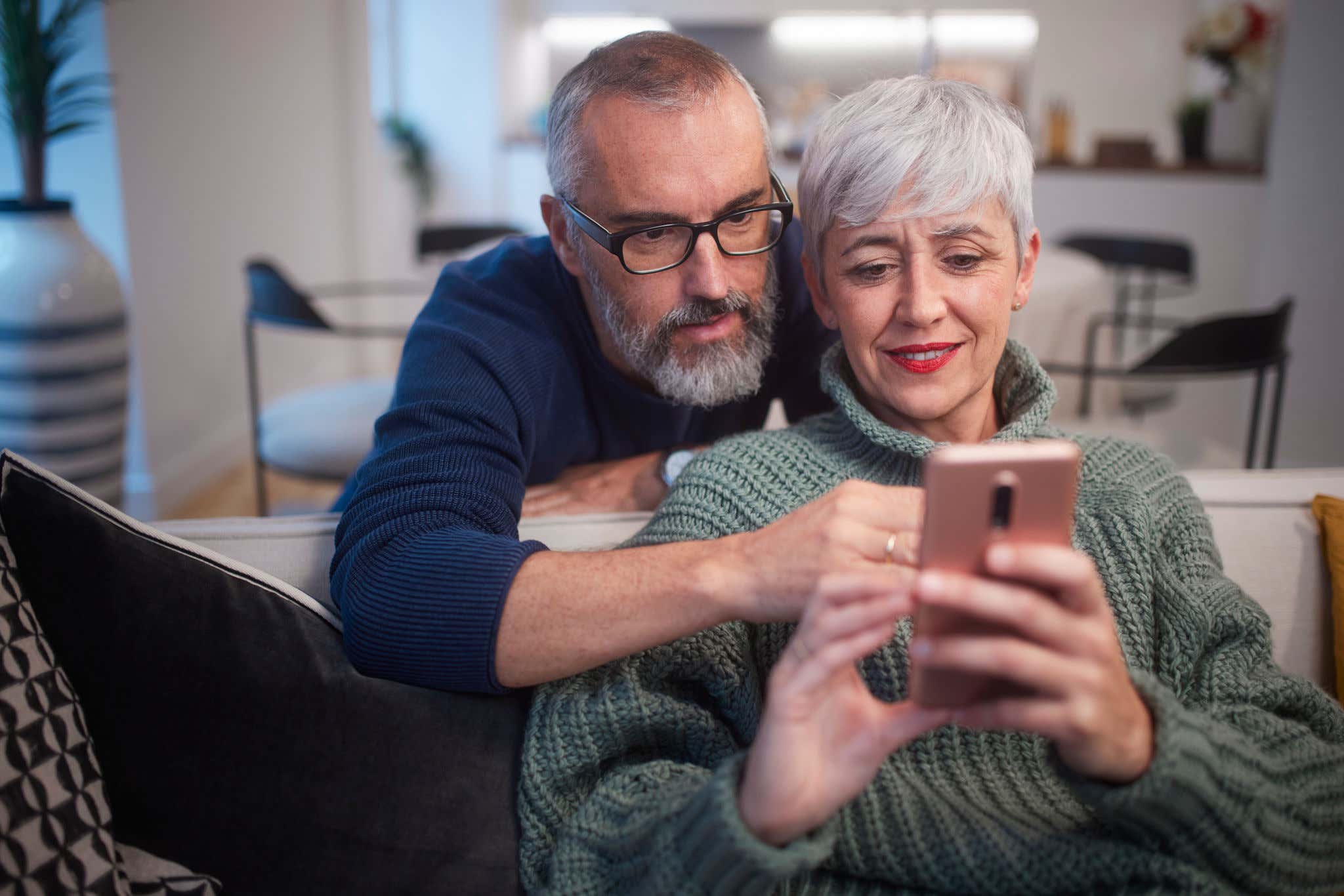 Close-up of senior woman showing smartphone to husband while sitting on sofa at home