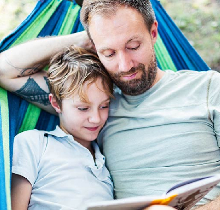 Father and son lying in hammock and reading a book together