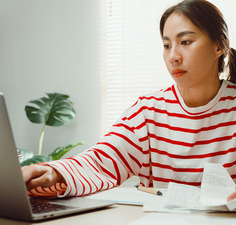 Woman wearing red and white striped top, sits at desk and types on laptop
