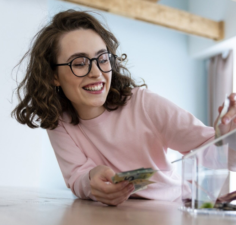 Woman wearing pink shirt and glasses placing money into a plastic house shaped money box