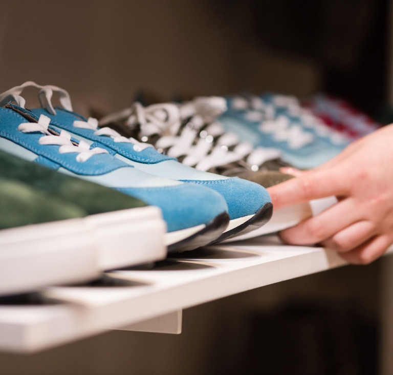 Hand reaching for pair of sneakers that is sat on shelf next to blue and green pairs of sneakers