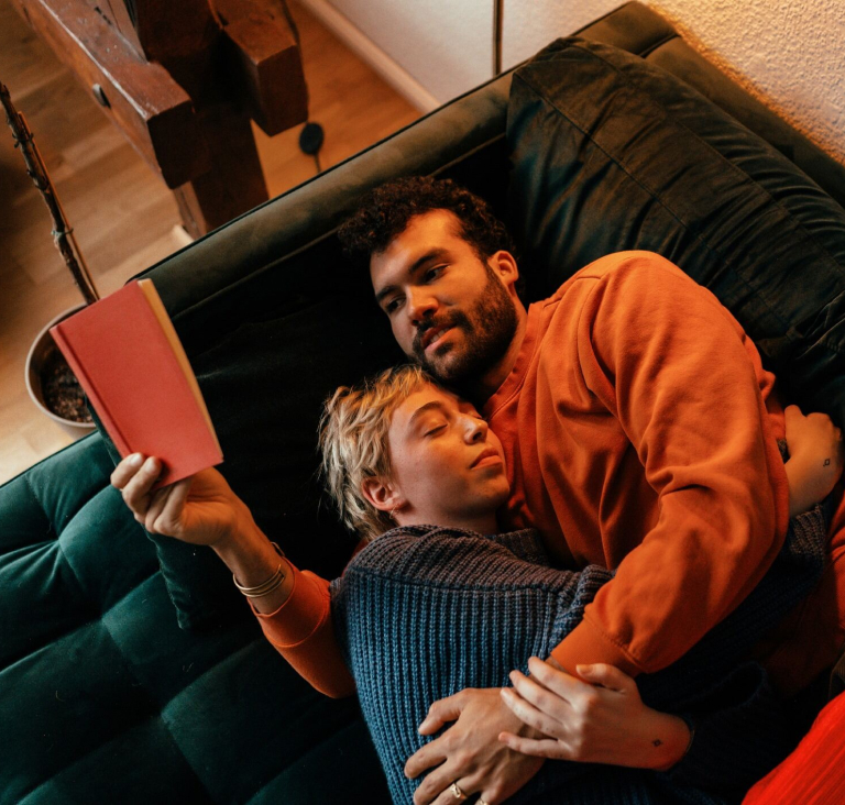 Couple lying on couch together, girl sleeps while boy reads book