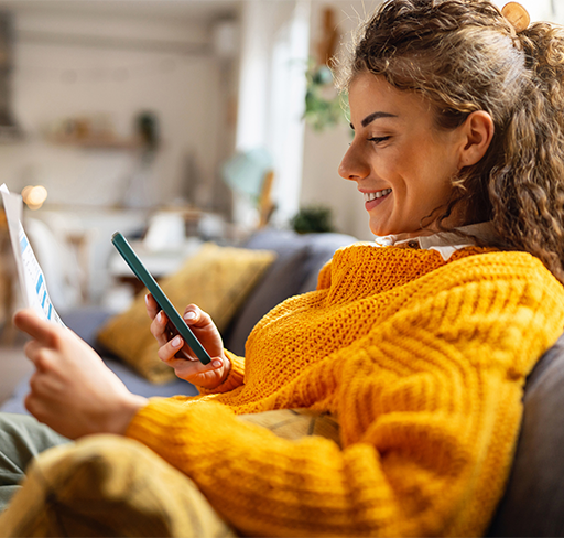 Smiling woman in sofa with phone and paper in hand