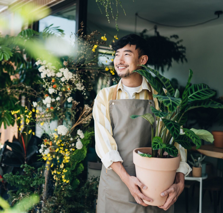 Man wearing apron holding a potted plant while standing in a flower shop