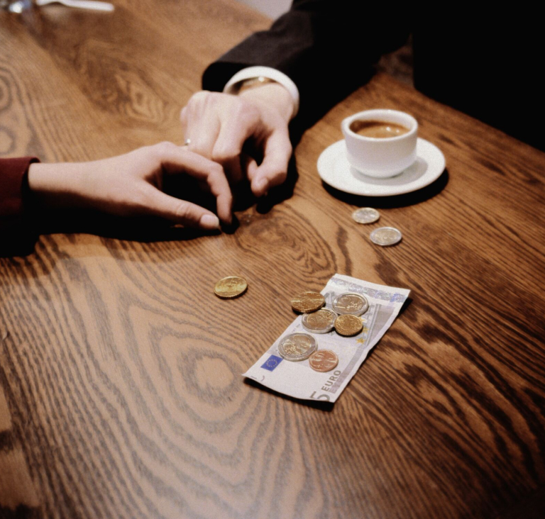 Two hands touching across table, next to single coffee cup and a small pile of cash