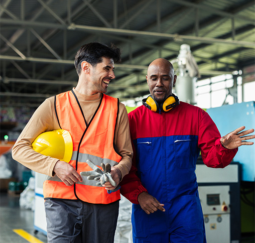 Two people wearing safety gear talk inside an industrial factory