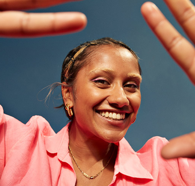 Close up of woman in pink shirt, holding her hands up to frame the image