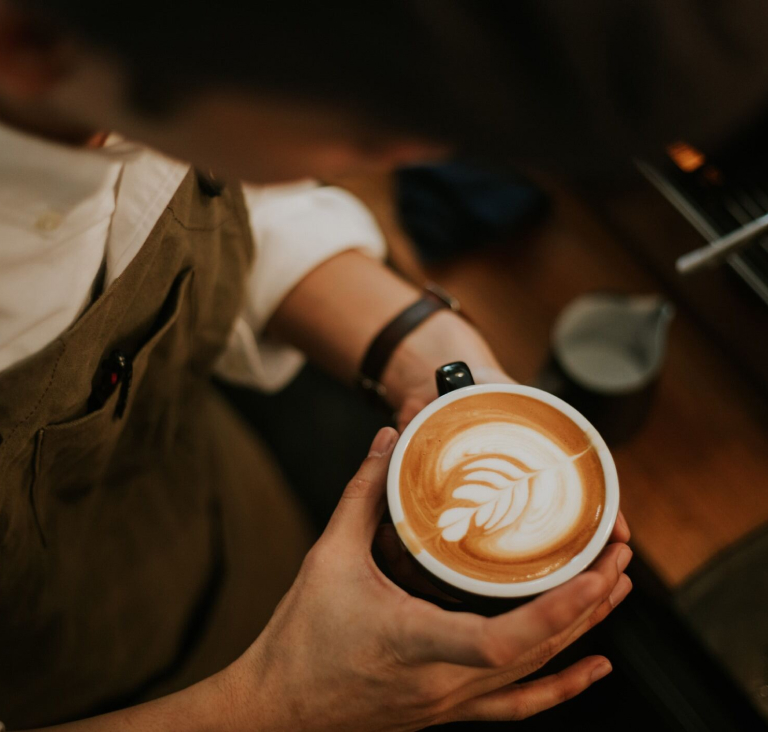 Close up of barista's hands holding coffee cup in front of coffee machine