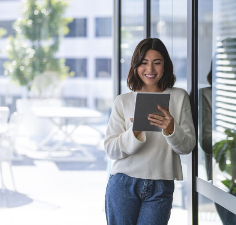Woman leaning against window outside holding ipad