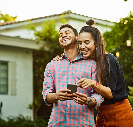 Young couple laughing watching phone outside the house