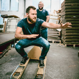 Person balancing on wooden boards in a warehouse while another person stands behind.