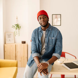 Person wearing a red beanie and denim shirt sitting at a table indoors.