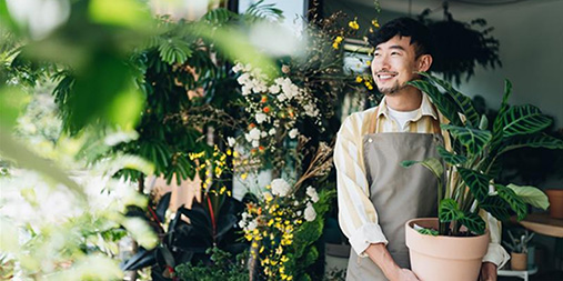 A florist holding a potted plant surrounded by lush greenery and flowers