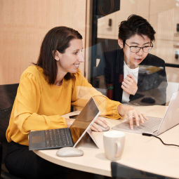 Two people collaborating at a table with laptops and a smartphone.
