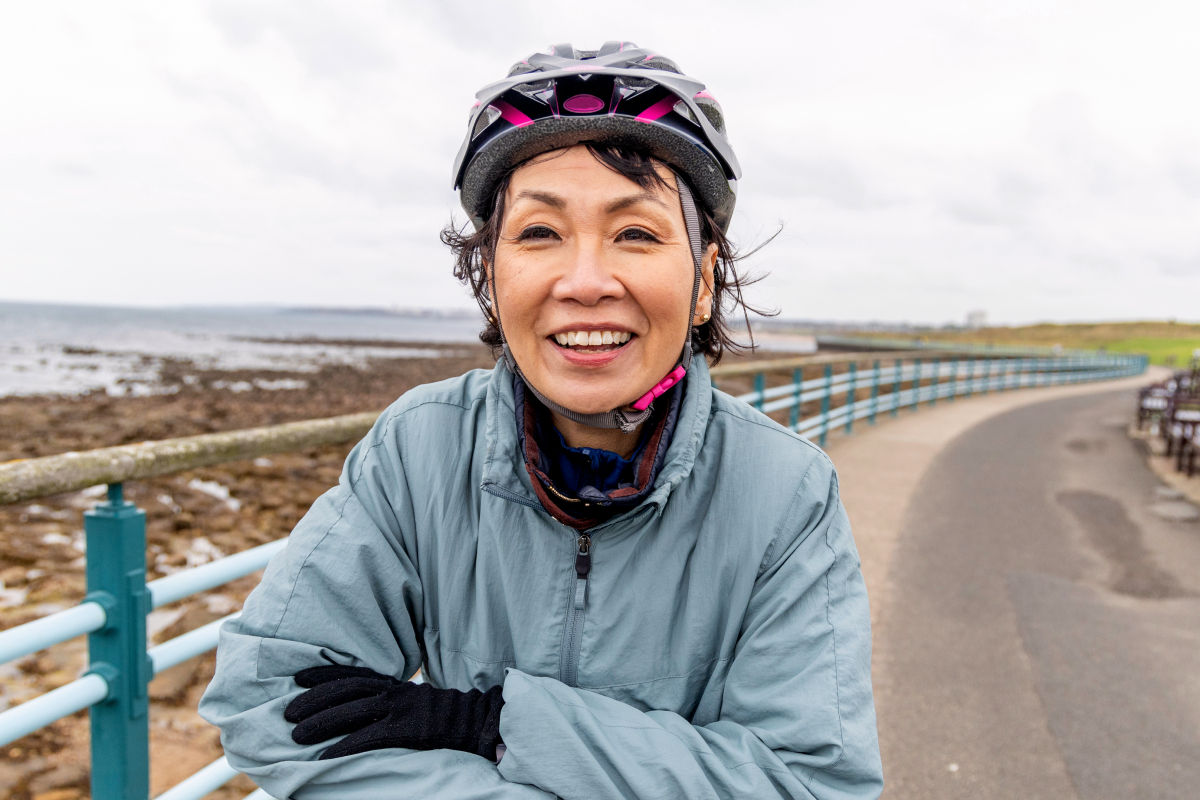 Woman with bike helmet, wearing a light blue jacket, smiling.