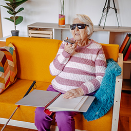 Person sitting on a sofa wearing glasses and using a laptop tray with a pen.