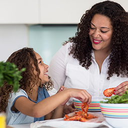 Adult and child preparing vegetables together in a kitchen.