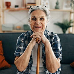 Older adult seated on a couch, holding a cane in a living room.