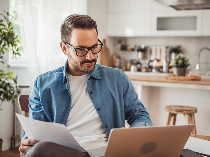 A person holding a paper and watching his laptop