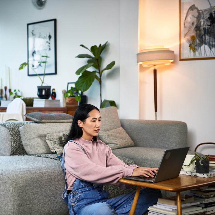 Person sitting on the floor using a laptop at a small table beside a couch.