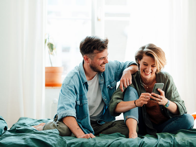 Couple sitting on bed looking at phone
