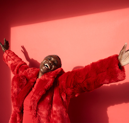 A woman in a red fake-fur coat raises her hands in happiness