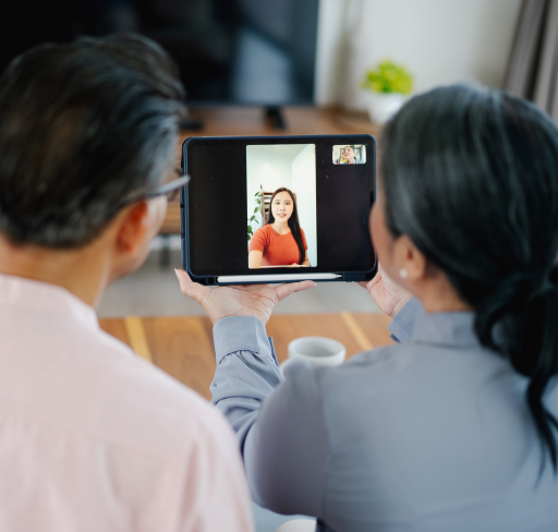 Two people hold a tablet displaying a video call with a person on screen in a home setting.