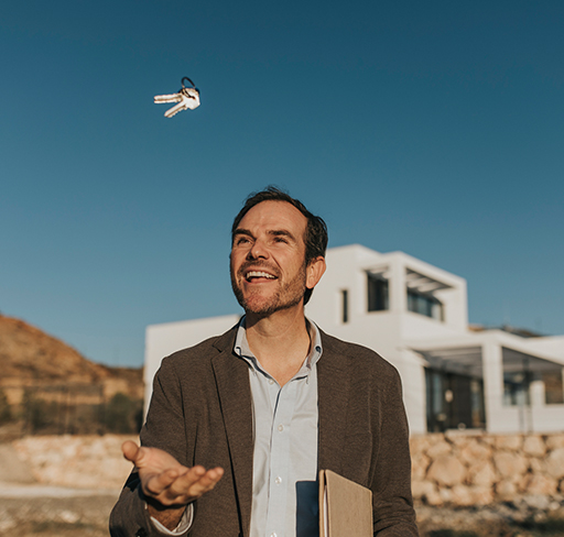 A person wearing a suit jacket holds a clipboard and tosses a set of keys into the air, with a modern house and a clear blue sky in the background.