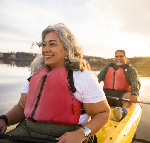 Two adults sitting in kayaks on calm water, wearing life jackets