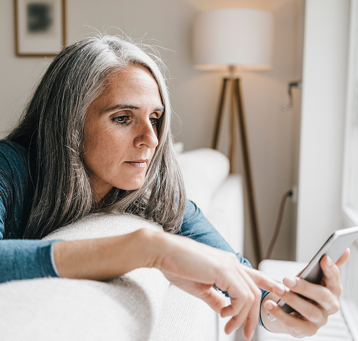 A woman looks at her phone while lying on a couch