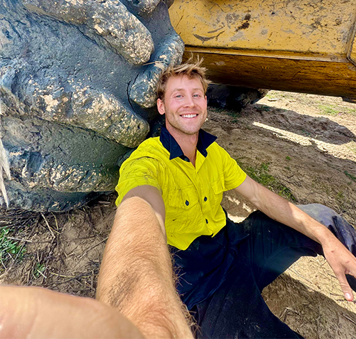 Woman in pink top and white pants stands inside a Pilates studio with reformers in the background