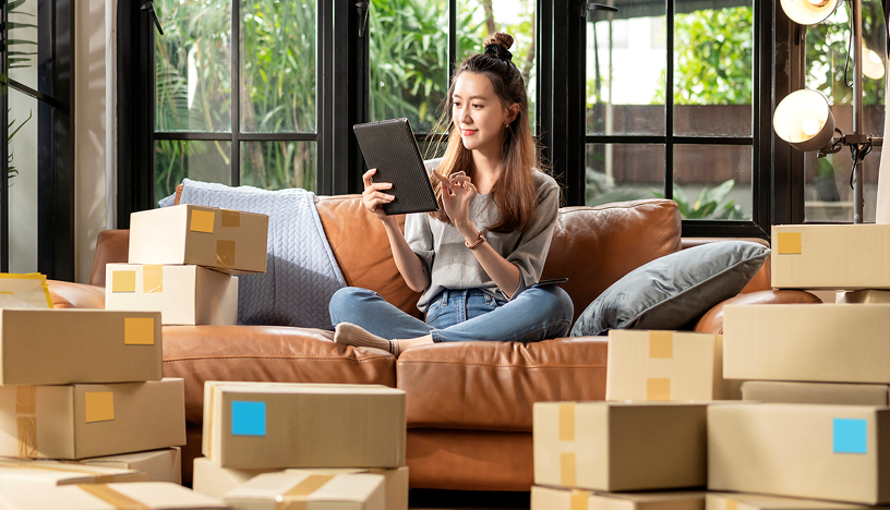 Women using ipad, sitting on sofa surrounded by boxes