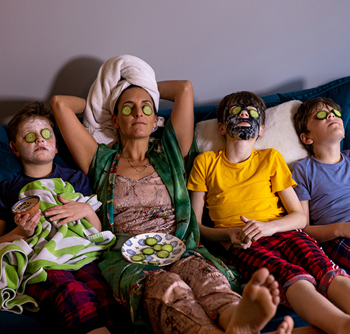 A mother and three sons lie on a couch with face masks and cucumbers over their eyes