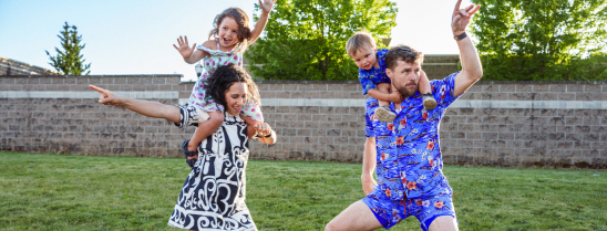 A couple with their kids on their shoulders dance in their backyard