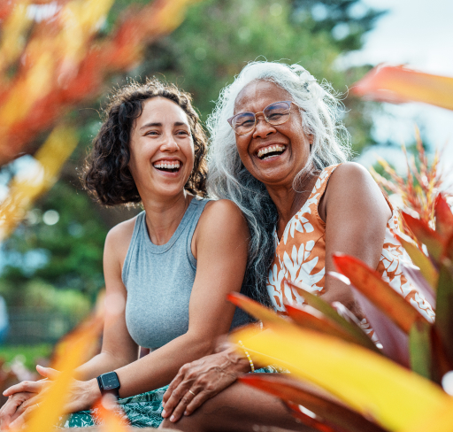 Two women sitting together in a garden setting, with plants in the foreground