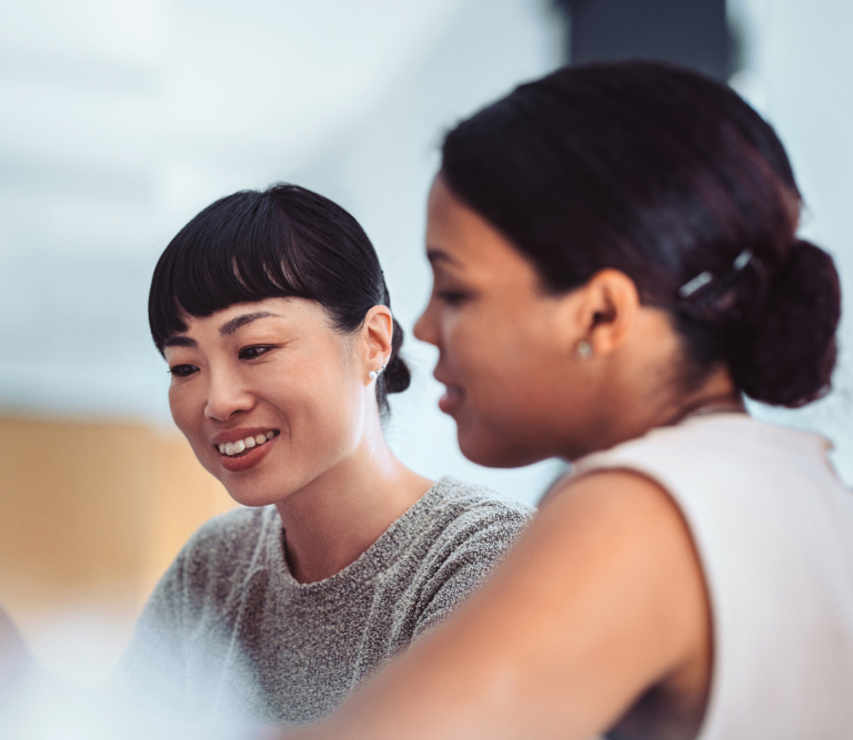 Two women seated together, looking down at a laptop