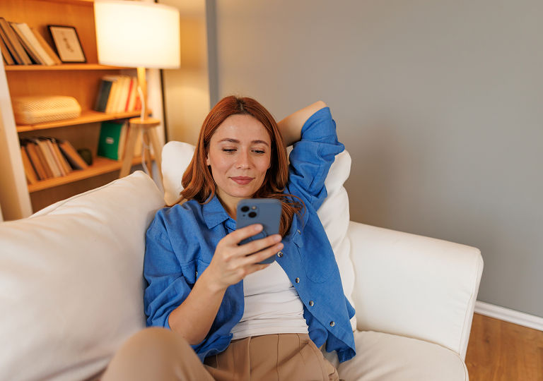 Woman wearing blue shirt, sat on sofa, looking at phone