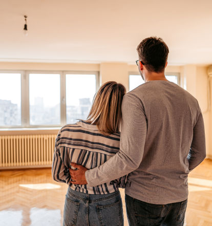 A young couple embrace as they look at a sun-drenched room.