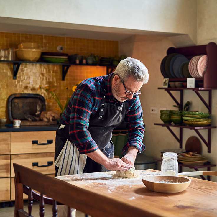 Older man kneading dough on kitchen table
